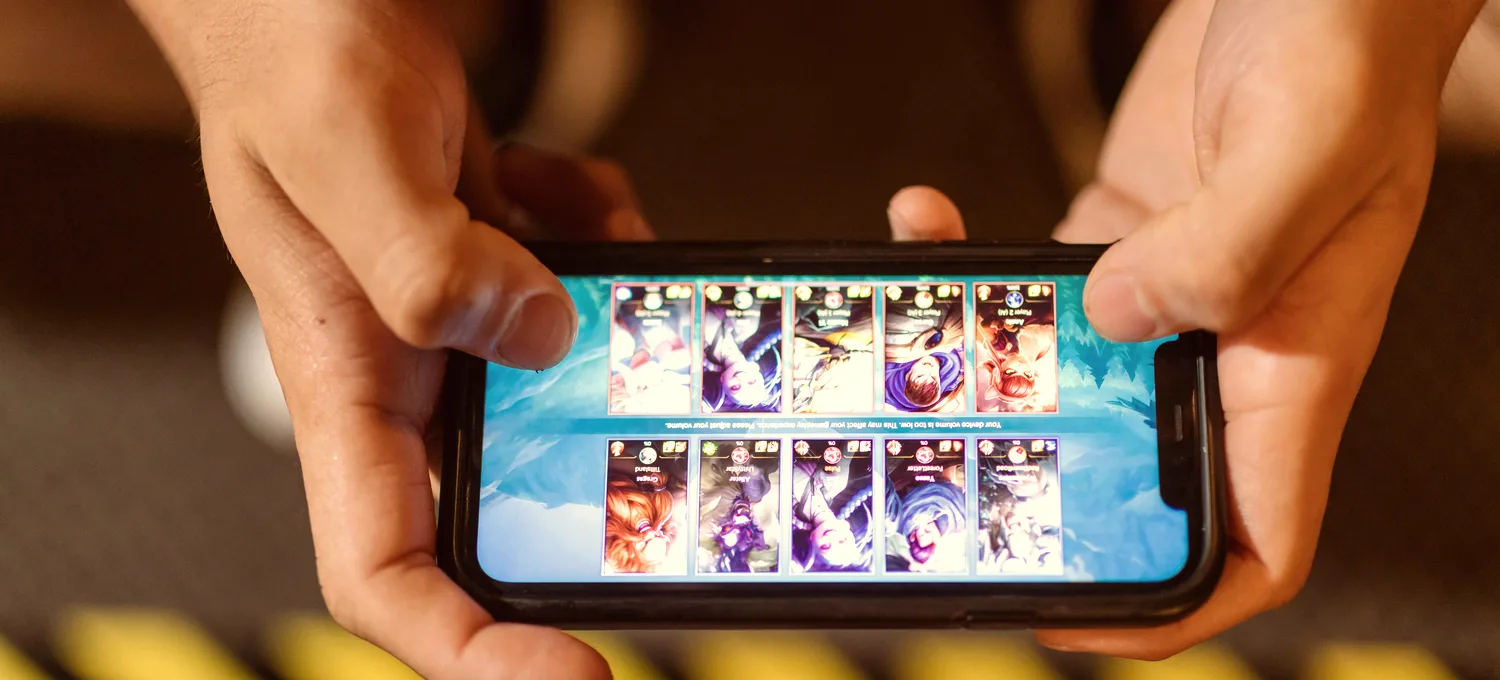 Hands holding a smartphone showing a card-based mobile game, warm indoor light